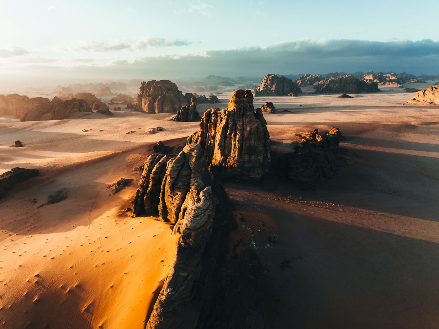 Aerial view of dramatic sandstone rock formations rising from golden desert sands in AlUla, Saudi Arabia