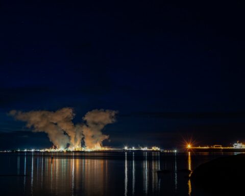 Oil refinery and tanker ship operations at night, representing Saudi Aramco wartime energy infrastructure