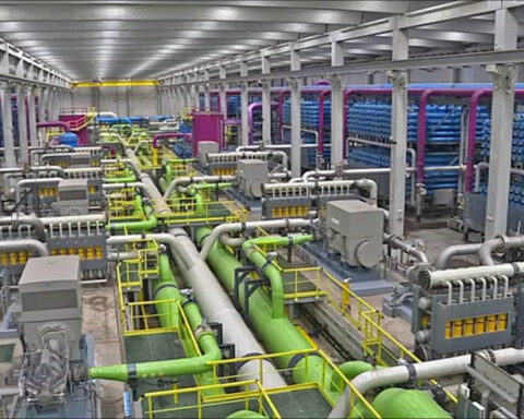 Interior of a large-scale seawater reverse osmosis desalination plant showing rows of blue membrane tubes and industrial piping systems that convert saltwater to drinking water