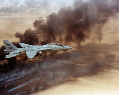 US Navy F-14 Tomcat fighter jet flying over burning Kuwaiti oil wells during the 1991 Gulf War, illustrating the devastating consequences of energy infrastructure targeted during armed conflict. Photo: US Navy / Public Domain