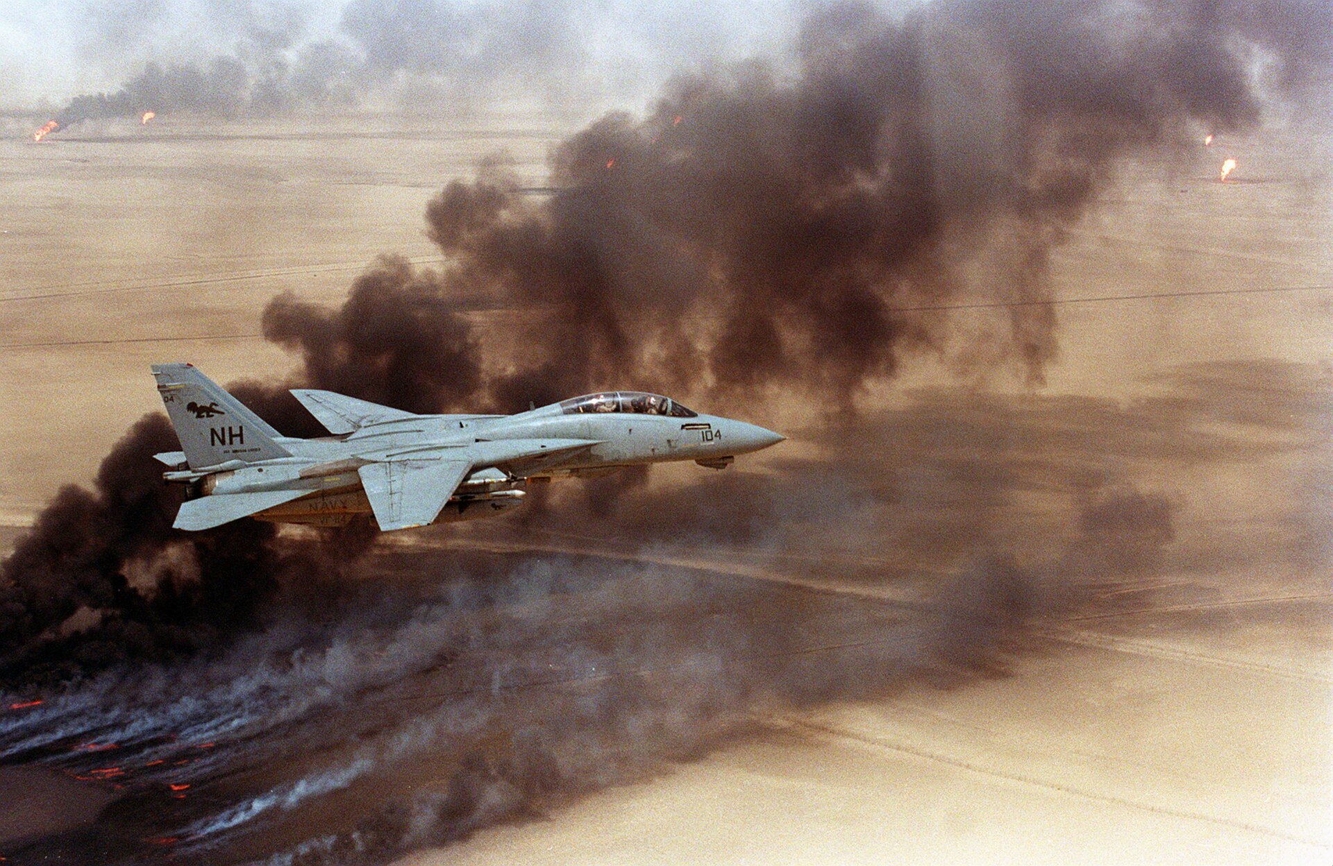 US Navy F-14 Tomcat fighter jet flying over burning Kuwaiti oil wells during the 1991 Gulf War, illustrating the devastating consequences of energy infrastructure targeted during armed conflict. Photo: US Navy / Public Domain