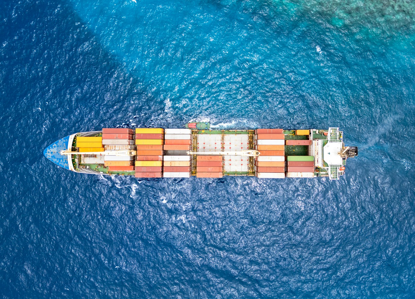 Aerial view of a container ship loaded with cargo navigating open water, illustrating global shipping disrupted by the Strait of Hormuz blockade