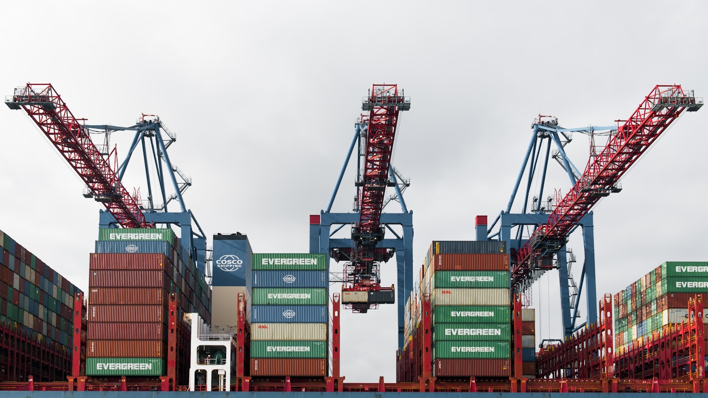Cargo cranes loading Evergreen and COSCO shipping containers at a port terminal as global trade reroutes away from the Strait of Hormuz