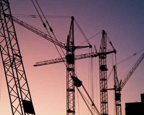 Tower cranes silhouetted against a twilight sky at a major construction site, representing the scale of Saudi Arabia's building boom now threatened by the Iran war
