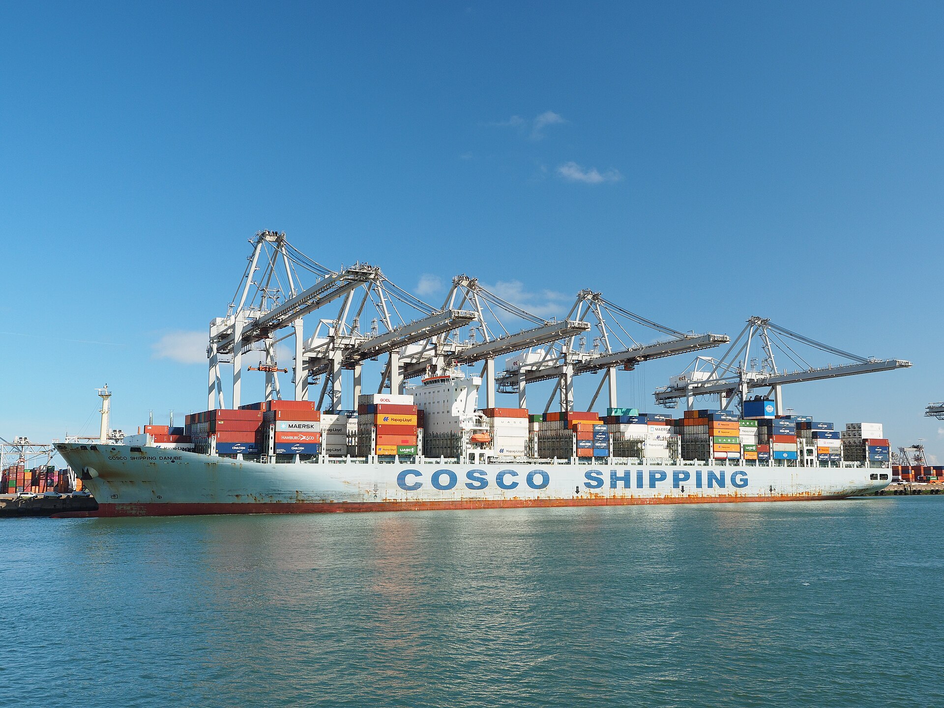 COSCO Shipping container vessel loaded with cargo containers at port with gantry cranes representing global petrochemical trade routes