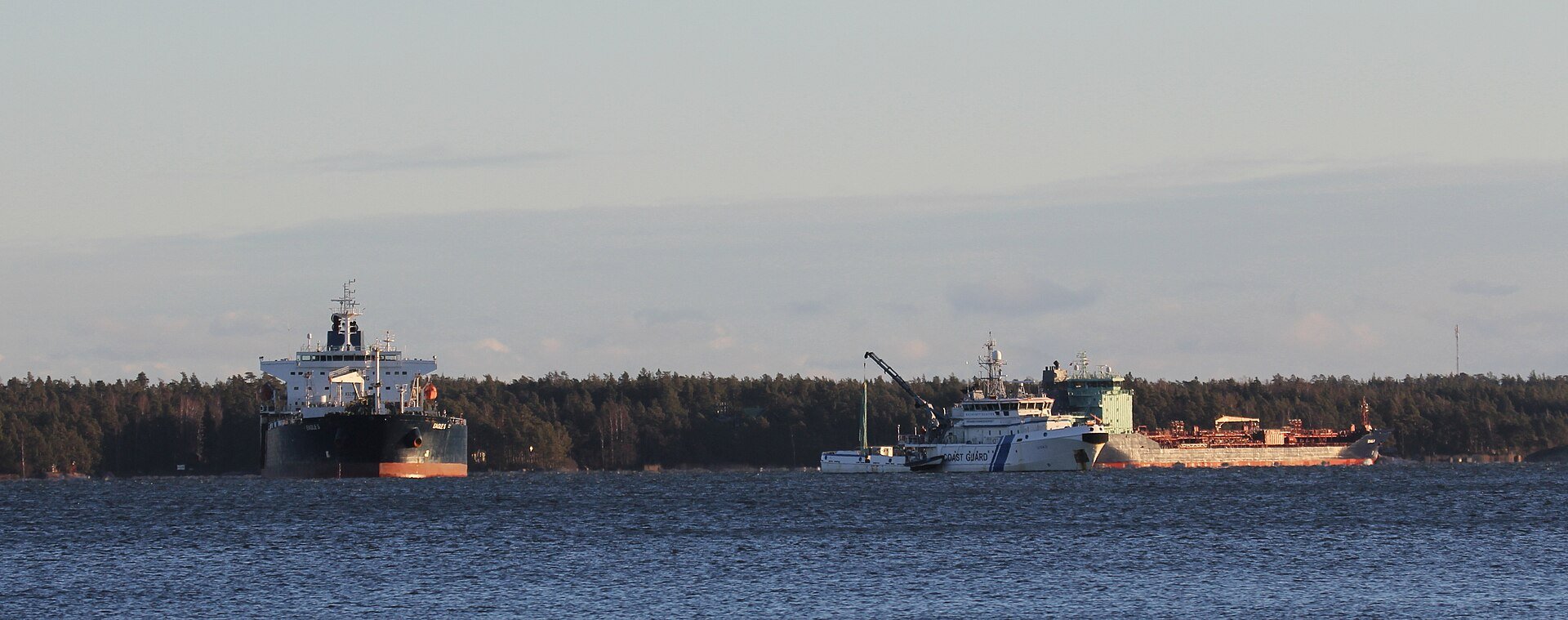 A crude oil tanker alongside a coast guard patrol vessel, illustrating the intersection of maritime commerce and state enforcement that defines the 2026 Hormuz insurance crisis. Photo: Wikimedia Commons / CC BY-SA 4.0
