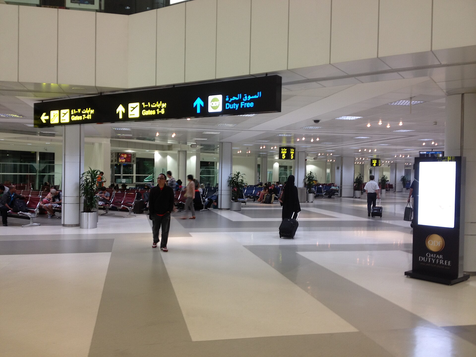 Passengers waiting in the departure terminal at Doha International Airport in Qatar with Arabic signage visible. Photo: Wikimedia Commons / CC BY-SA 4.0