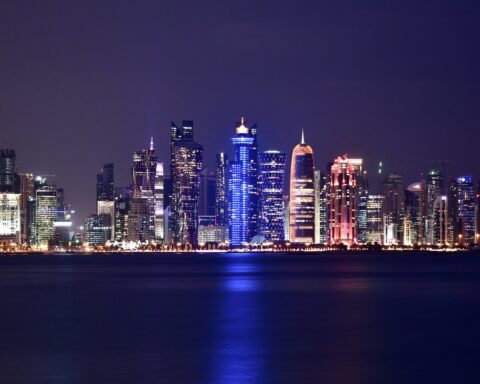 Doha West Bay financial district skyline at night, representing Gulf economies facing their worst economic crisis since 1990 as the Iran war threatens GDP across Qatar, Kuwait, UAE, and Saudi Arabia. Photo: Thameur Belghith, CC BY-SA 4.0, via Wikimedia Commons
