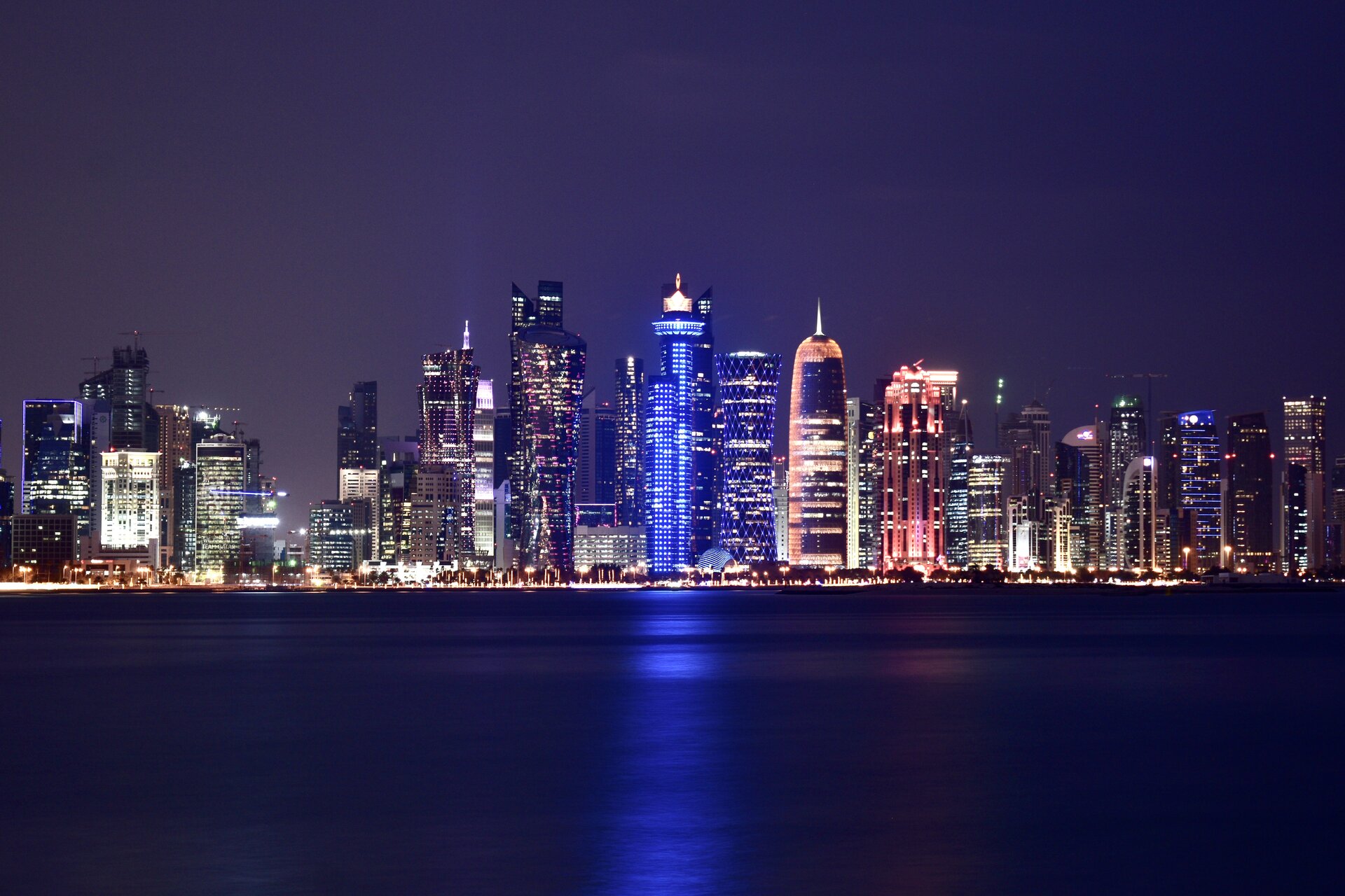 Doha West Bay financial district skyline at night, representing Gulf economies facing their worst economic crisis since 1990 as the Iran war threatens GDP across Qatar, Kuwait, UAE, and Saudi Arabia. Photo: Thameur Belghith, CC BY-SA 4.0, via Wikimedia Commons