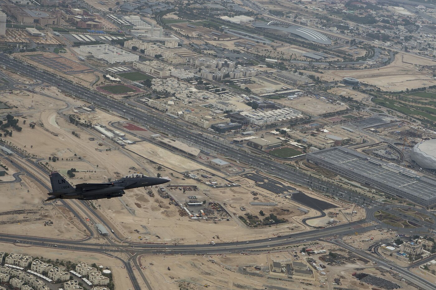 Aerial view of Qatar Education City campus complex in Al Rayyan with a U.S. Air Force F-15E Strike Eagle flying overhead during a formation flyover
