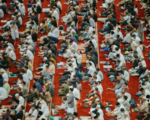 Thousands of Muslim worshippers gathered for Eid al-Fitr prayer in a grand mosque, seated on red carpets in rows during the 2026 wartime celebration
