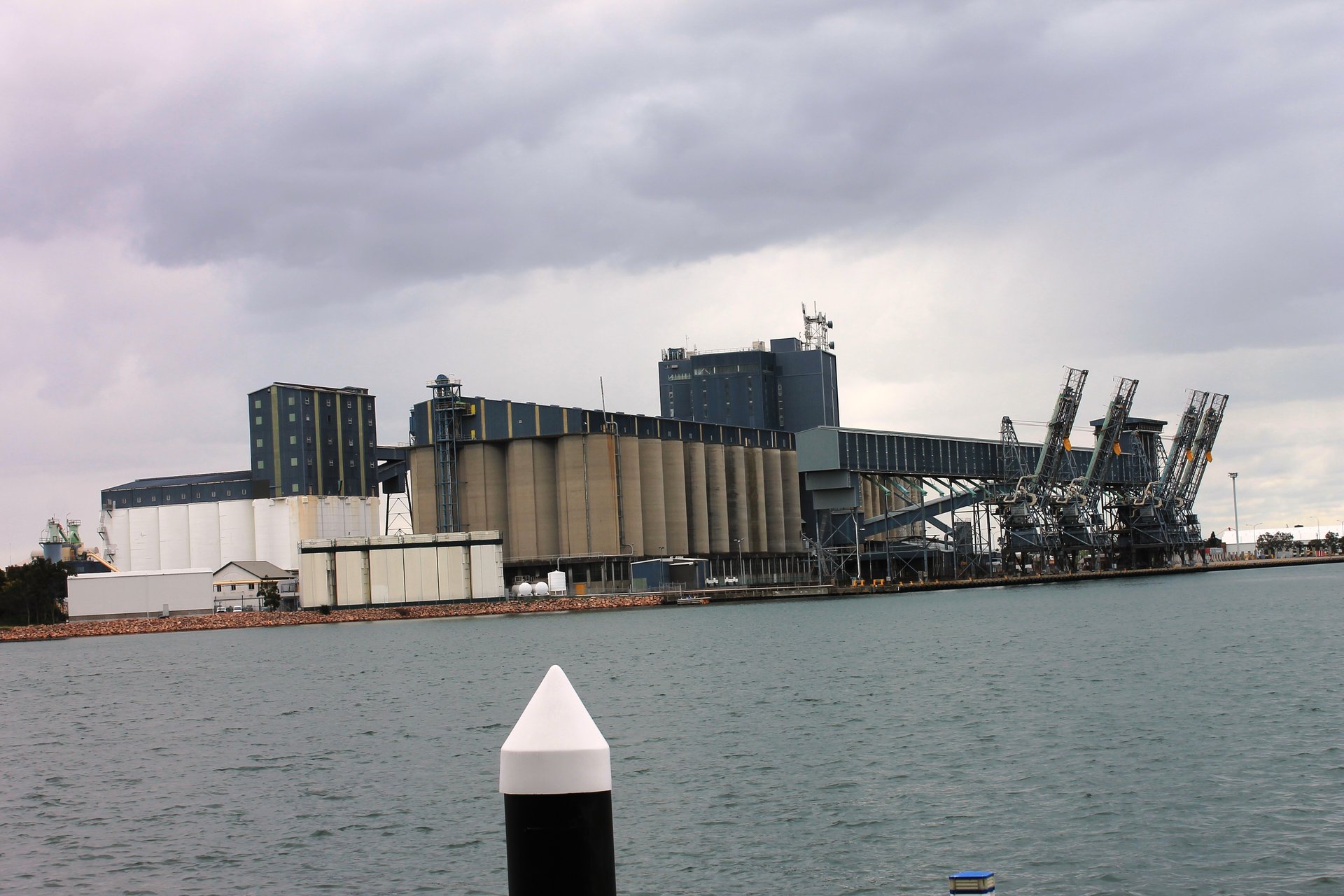 Port grain silos and bulk wheat storage facility at harbour with cargo ship alongside