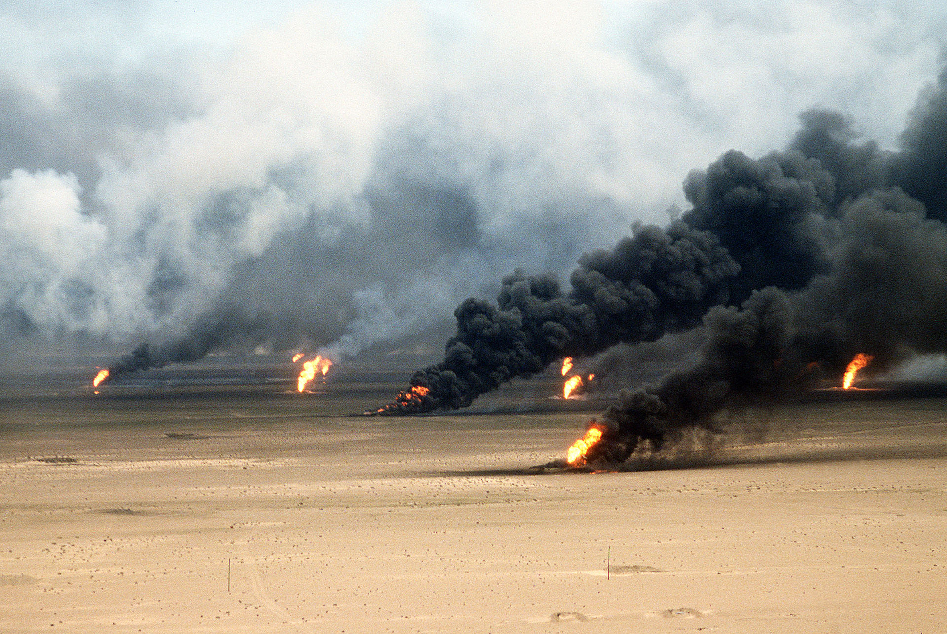 Oil well fires burning across a desert landscape with massive black smoke plumes rising into the sky, illustrating the destruction of Gulf energy infrastructure. Photo: US Department of Defense / Public Domain
