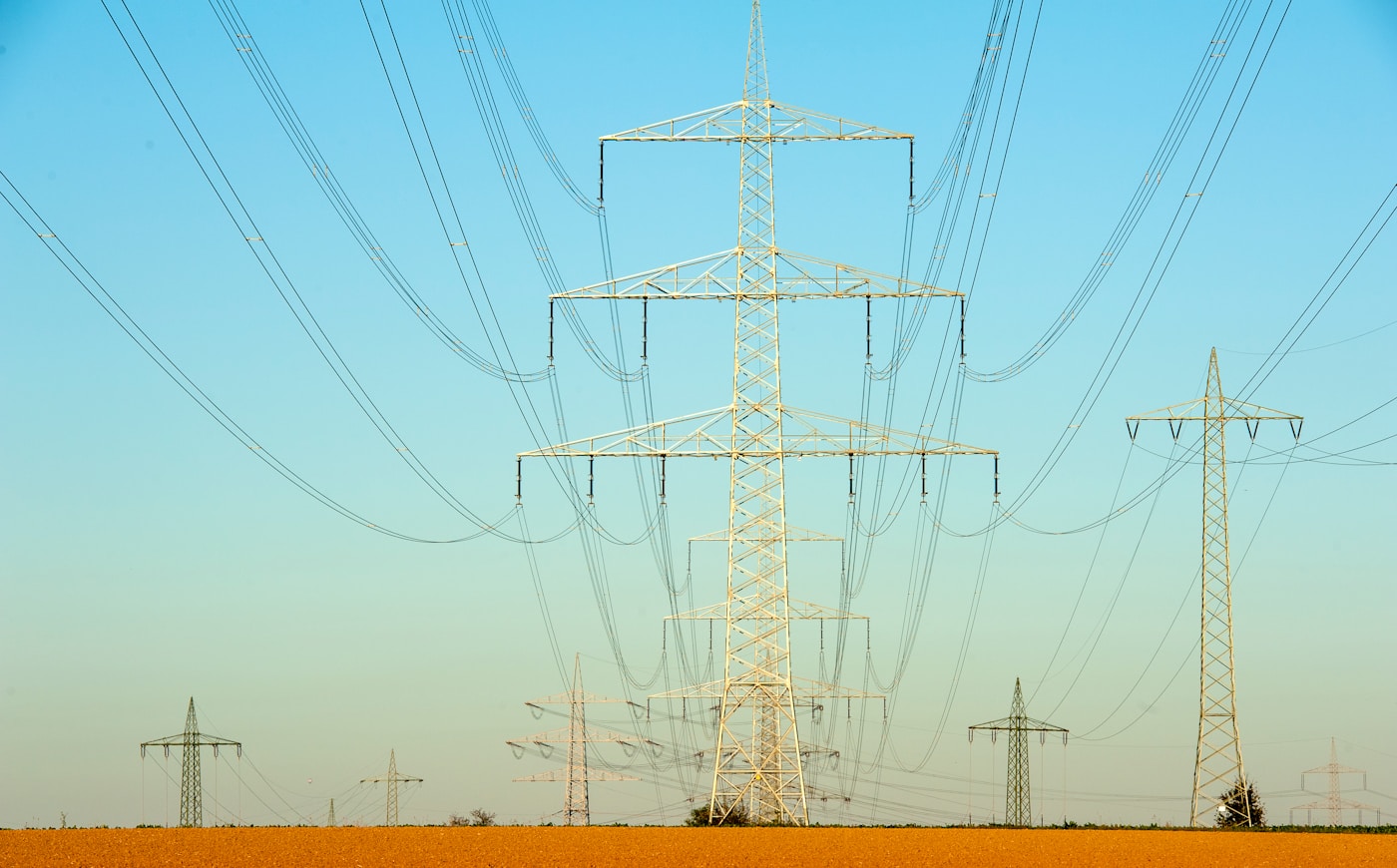 High-voltage electricity transmission towers and power lines stretching across an agricultural landscape, representing the fragile energy infrastructure serving developing nations