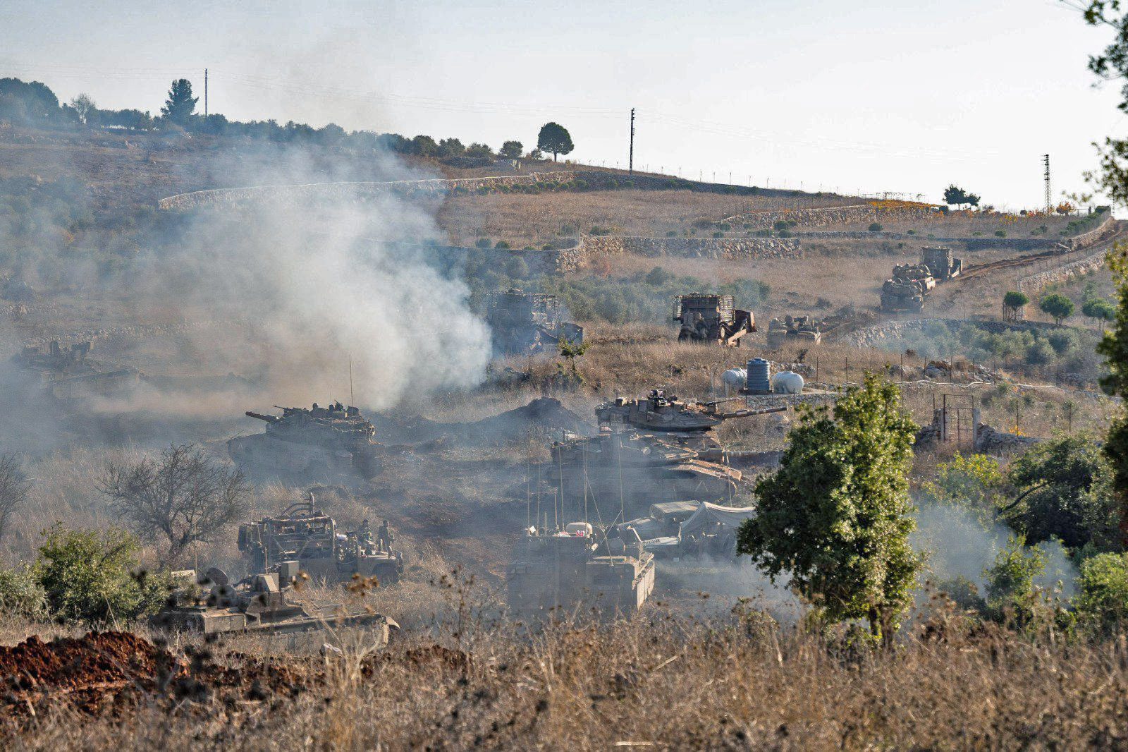 Israeli armored vehicles and tanks advance through southern Lebanon during ground operations, with smoke rising from the hillside. Photo: IDF / Wikimedia Commons / CC BY-SA 3.0
