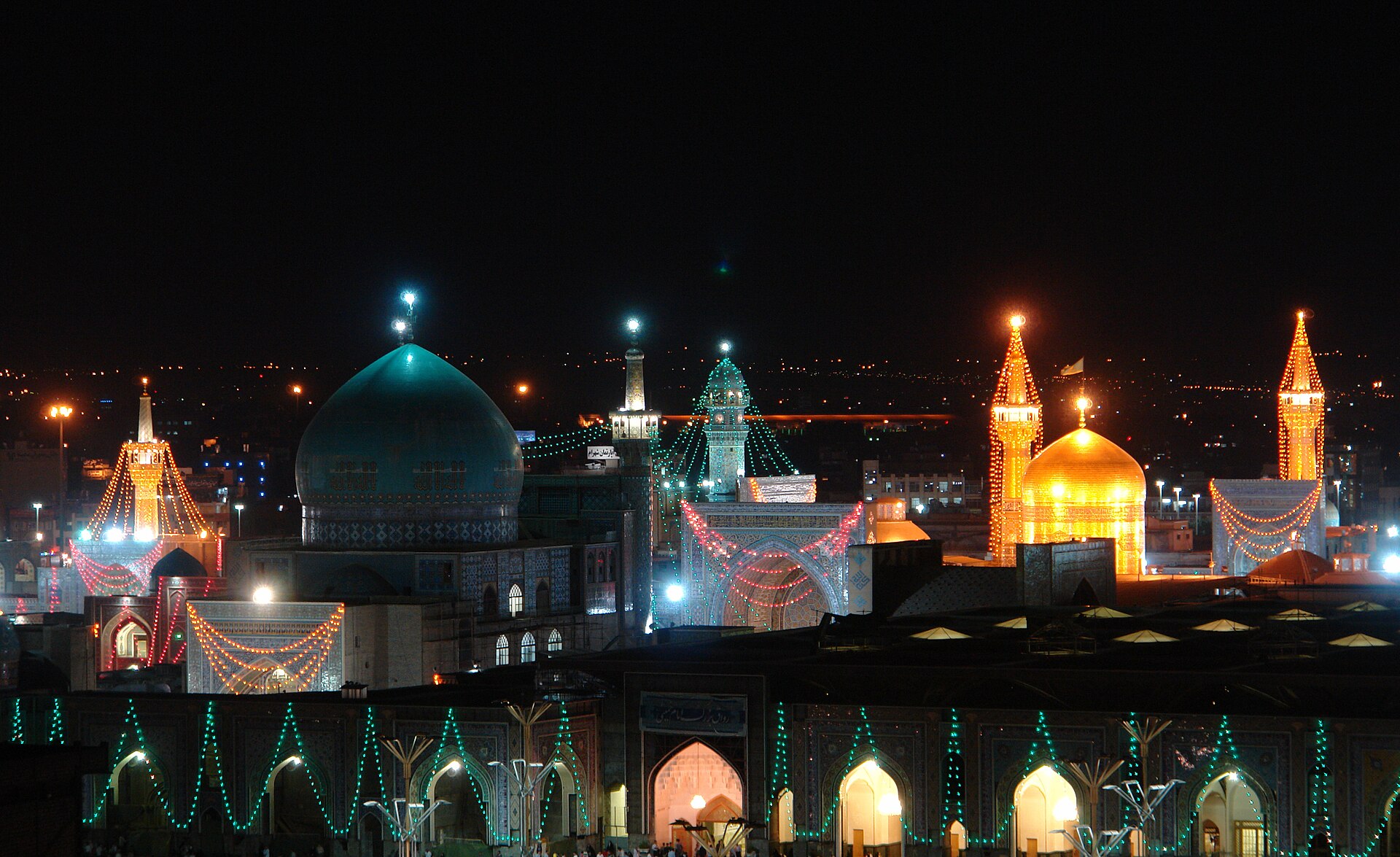 The Imam Reza shrine in Mashhad, Iran, illuminated at night with golden and turquoise domes, one of Shia Islam's holiest pilgrimage sites