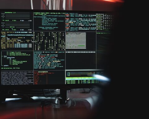 Computer terminal displaying system error logs and security alerts during a cyber warfare operation, with red accent lighting illuminating the monitoring station