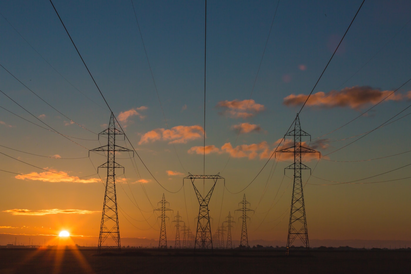 High-voltage power transmission towers silhouetted against a sunset sky, representing the electrical grid infrastructure threatened by Trump 48-hour ultimatum against Iran