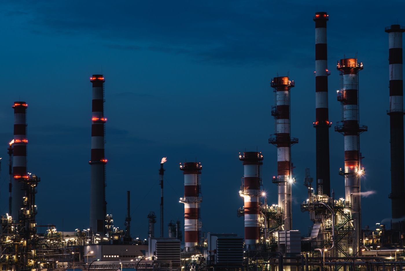 Oil refinery stacks illuminated at night, representing the petrochemical infrastructure that depends on Saudi Arabian crude oil supply