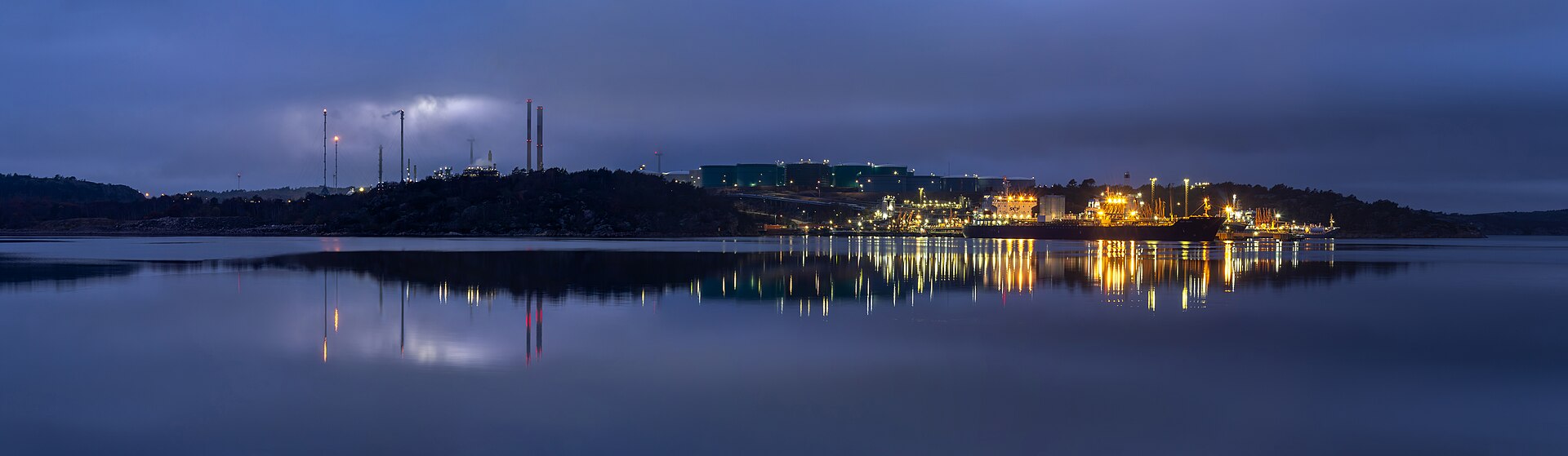 An oil refinery and petroleum infrastructure illuminated at dusk, representing energy assets whose insurance coverage has been revoked amid the Iran war