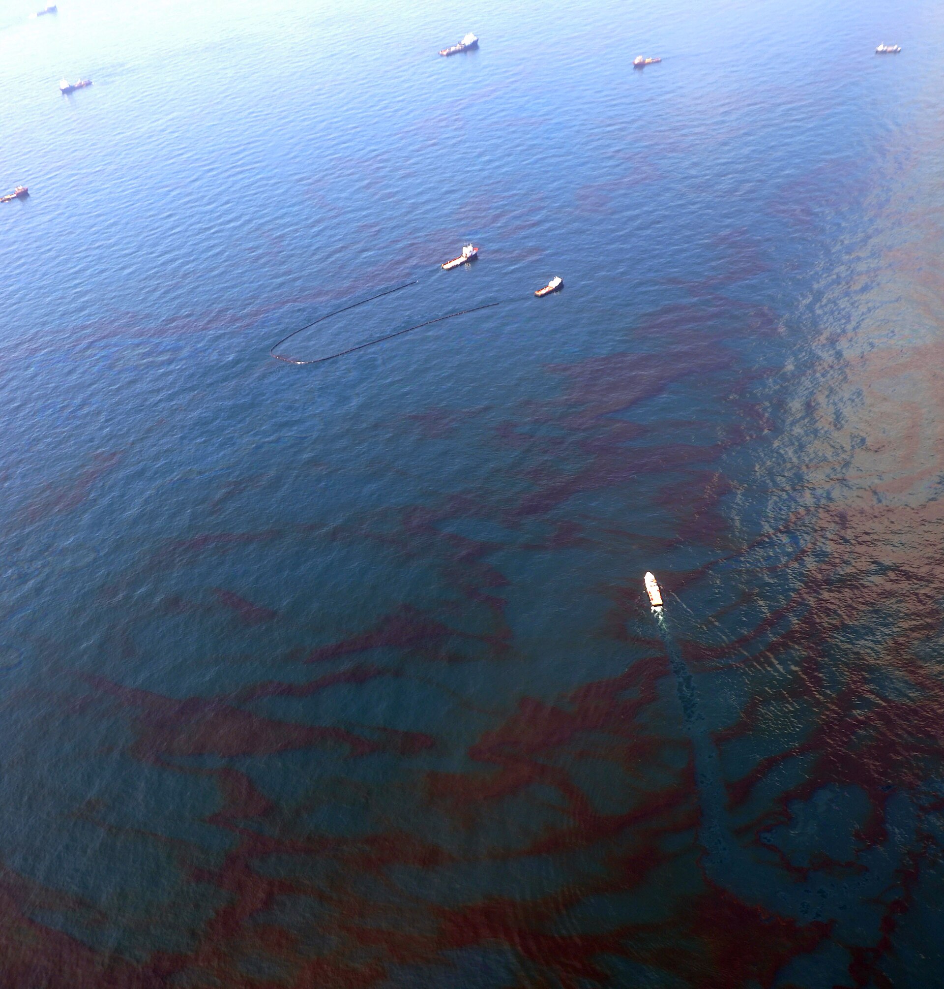 Aerial view of oil-contaminated waters with cleanup vessels attempting to skim crude oil from the sea surface, illustrating the environmental threat facing the Persian Gulf. Photo: US Coast Guard / CC BY 2.0
