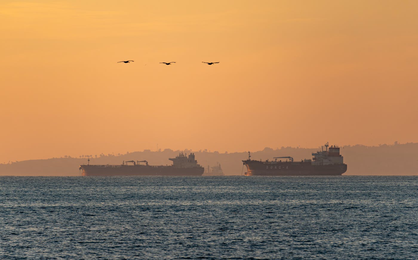 Oil tankers silhouetted at sunset on open water, symbolizing the disruption to global crude oil shipping caused by the Strait of Hormuz closure