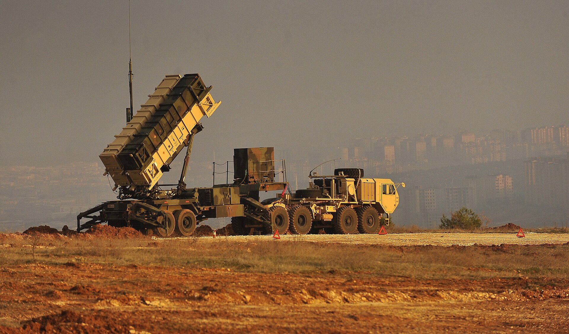US Patriot missile defense battery positioned at an elevated position overlooking a city, part of the air defense systems deployed across the Gulf to intercept Iranian drone and missile attacks. US Army / Public Domain