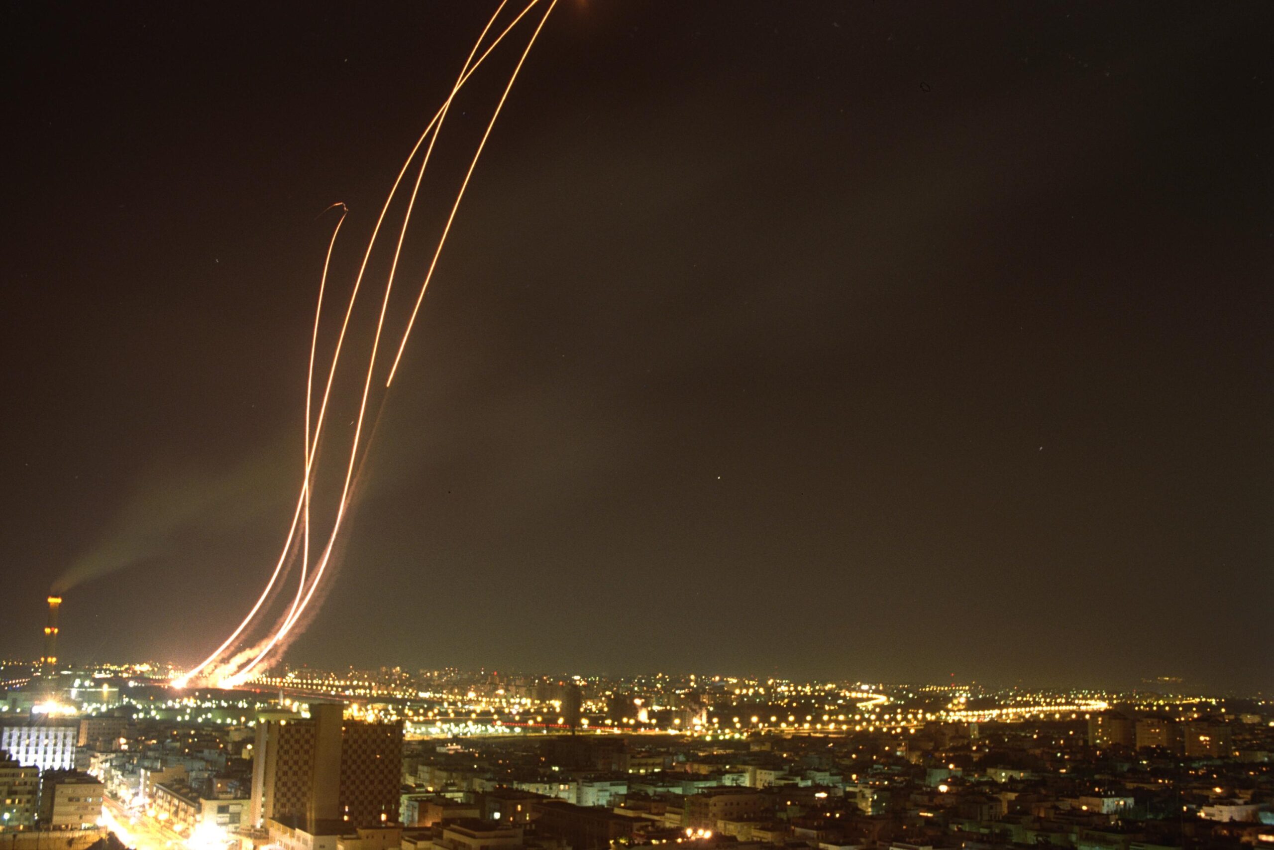Patriot missile interceptors launching at night over a city, streaking across the sky to intercept incoming missiles during the 2026 Iran war. Photo: Government Press Office / CC BY-SA 3.0
