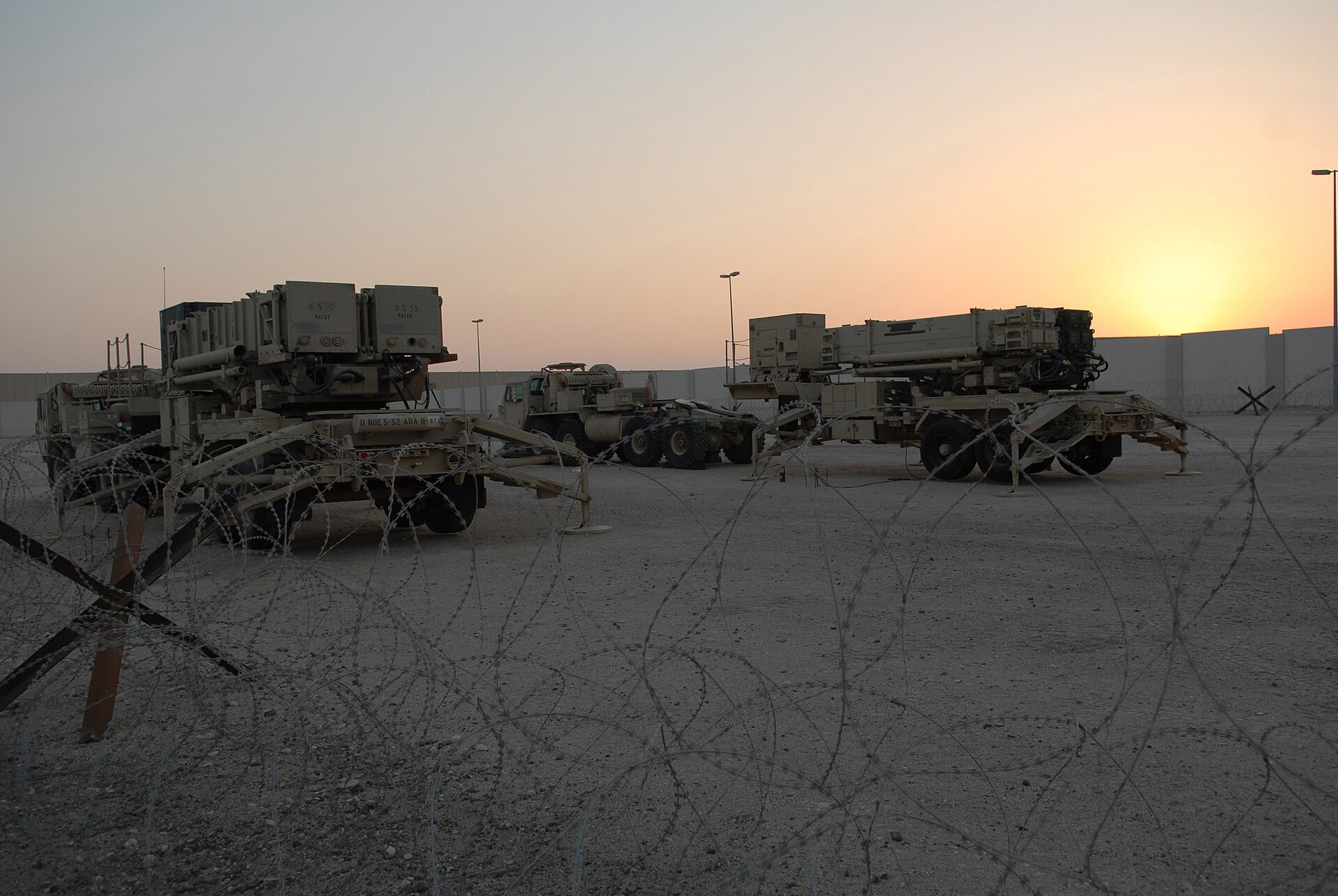 PAC-2 and PAC-3 Patriot missile launchers deployed at an air base in Southwest Asia at sunset behind concertina wire