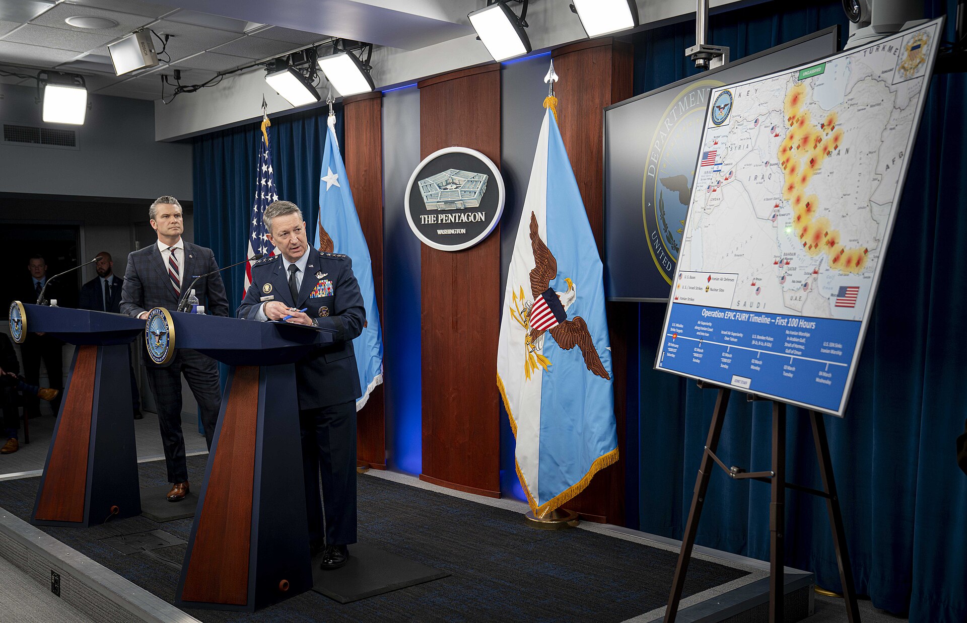 Secretary of War Pete Hegseth and Joint Chiefs Chairman Gen. Dan Caine brief reporters at the Pentagon on Operation Epic Fury, with a strike map of Iran visible. Photo: Department of War / CC BY 4.0