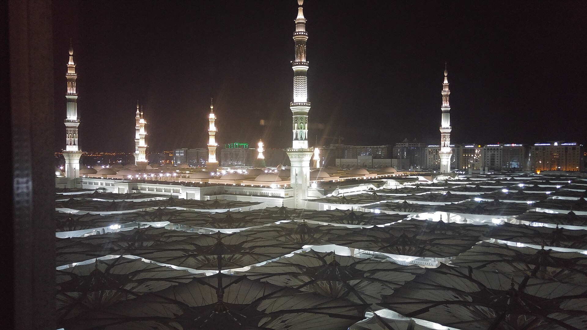 The Prophet's Mosque in Madinah illuminated at night with its distinctive retractable umbrella canopies and minarets during Ramadan