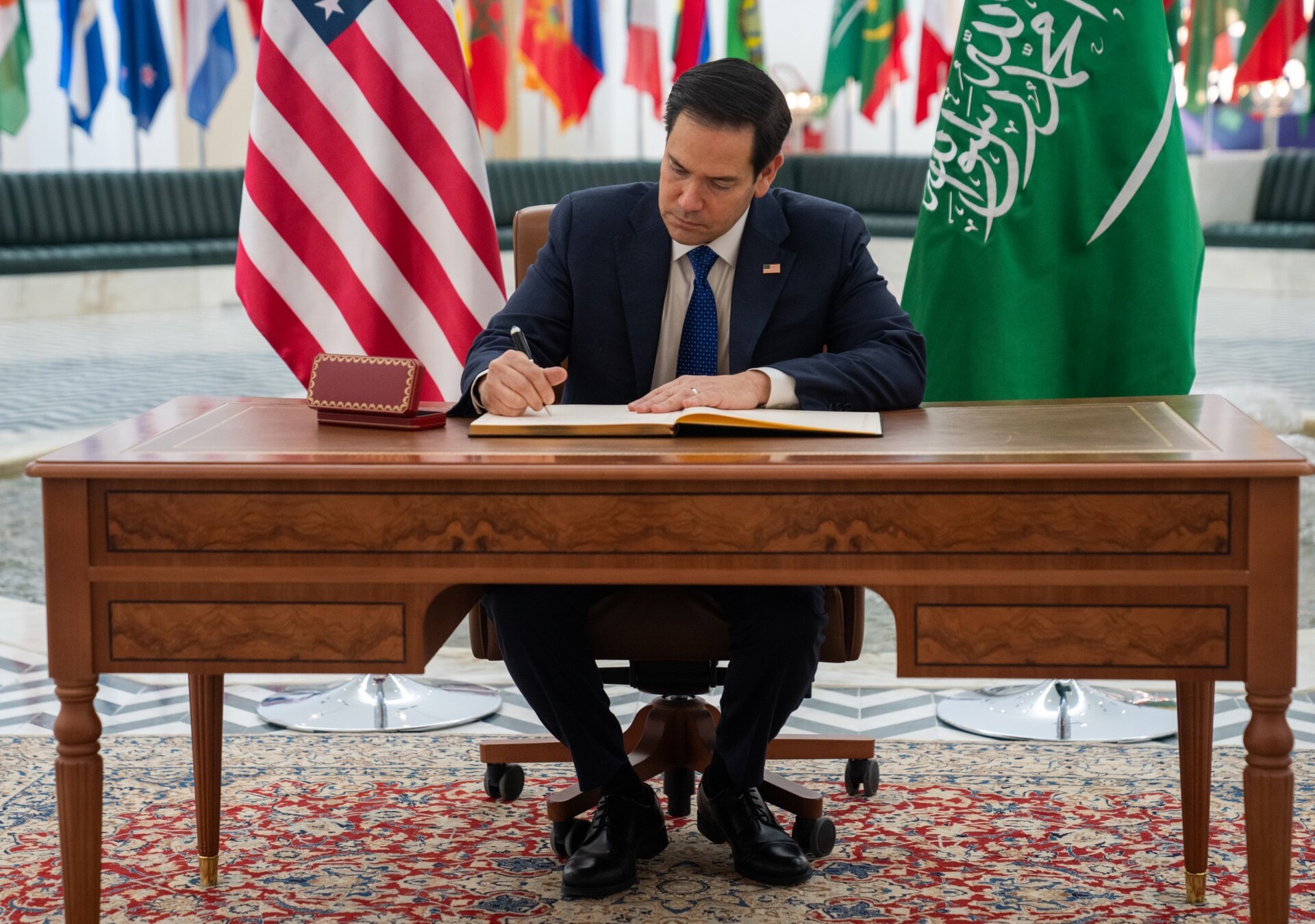 US Secretary of State Marco Rubio signs the guest book at the Saudi Foreign Ministry in Riyadh, with US and Saudi flags visible. Photo: US State Department / Public Domain
