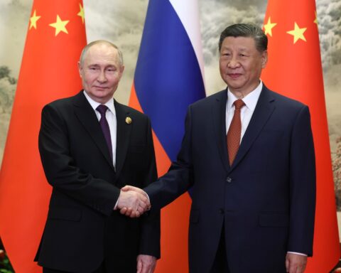 Russian President Vladimir Putin and Chinese President Xi Jinping shake hands during a 2024 bilateral meeting, with Russian and Chinese flags behind them. Photo: Kremlin.ru / CC BY 4.0