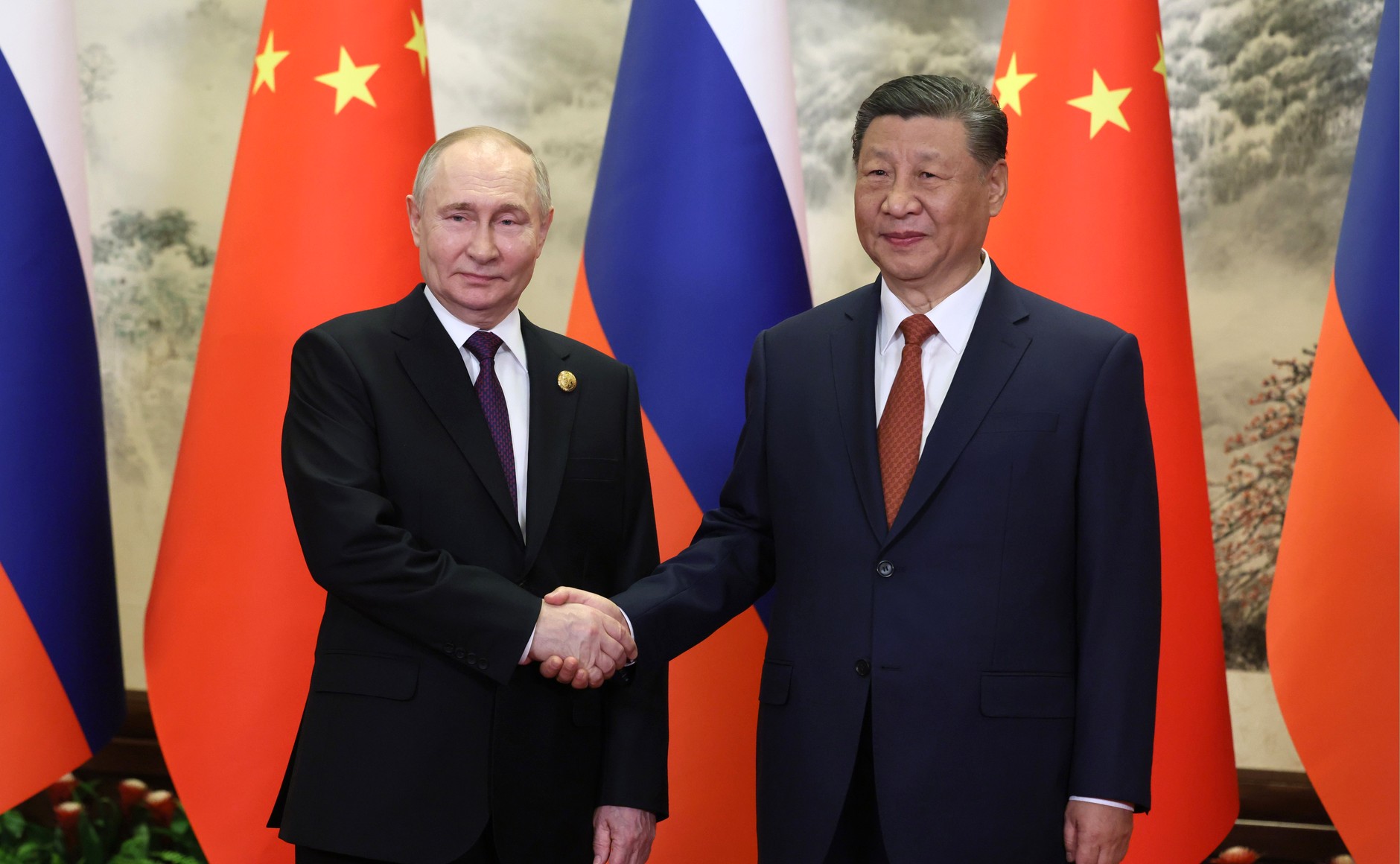 Russian President Vladimir Putin and Chinese President Xi Jinping shake hands during a 2024 bilateral meeting, with Russian and Chinese flags behind them. Photo: Kremlin.ru / CC BY 4.0