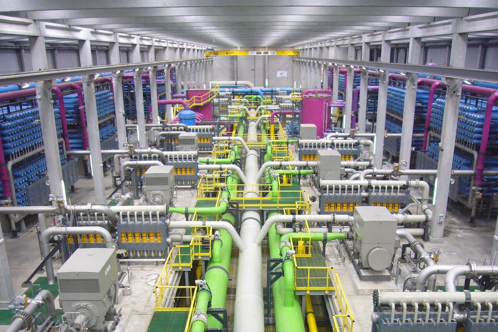 Interior of a large-scale reverse osmosis desalination plant showing green industrial pipes and membrane filtration racks used to produce drinking water from seawater. Photo: Wikimedia Commons / CC BY-SA 3.0