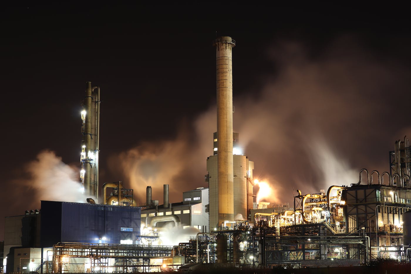 An oil refinery operating at night with steam rising from industrial processing towers, representing the type of energy infrastructure targeted by Iranian cyber operations against Saudi Arabia