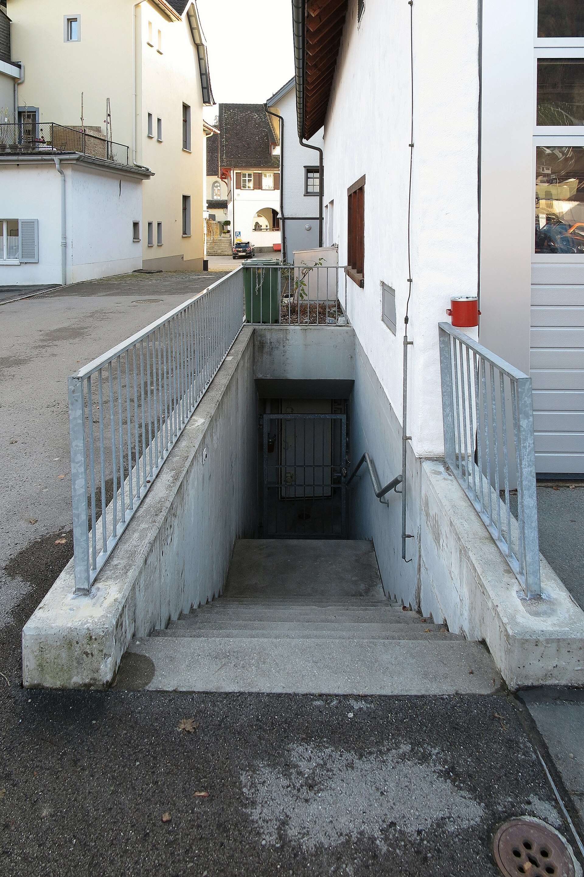 Entrance to a Swiss civil defense bunker built into residential buildings in Berneck, Switzerland, showing concrete steps leading to an underground shelter. Photo: Wikimedia Commons / CC BY 2.0