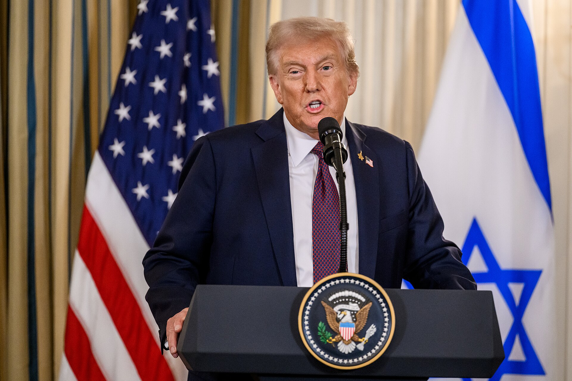 President Donald Trump speaks at a press conference at the White House flanked by US and Israeli flags. Photo: White House / Public Domain