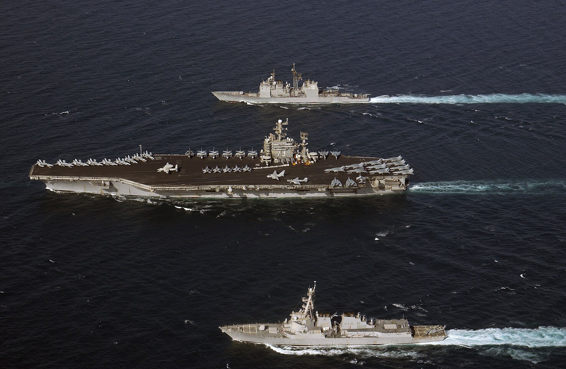 A US Navy carrier strike group with destroyer and cruiser escorts, representing the naval convoys proposed to reopen the Strait of Hormuz
