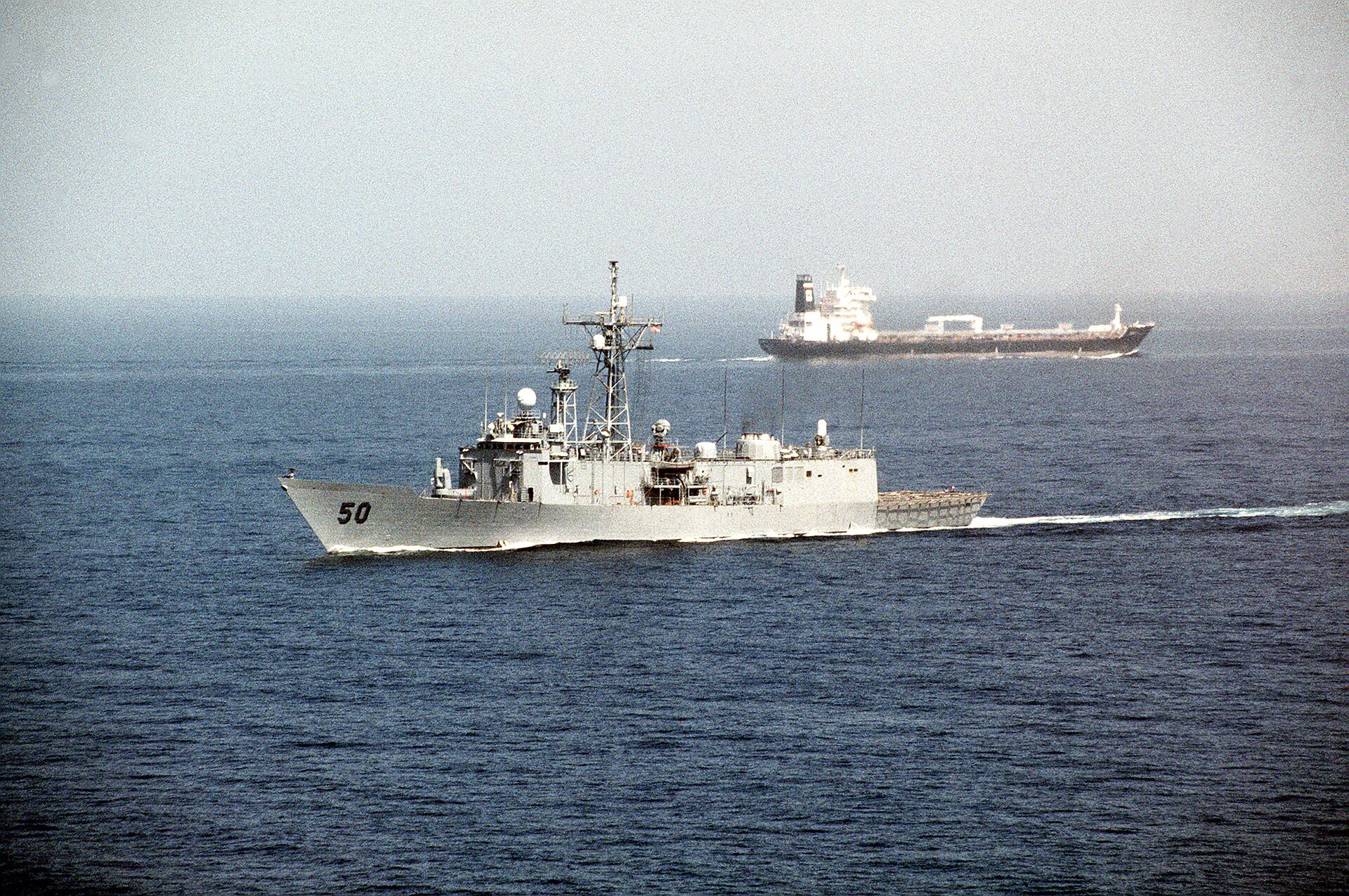 USS Taylor guided missile frigate escorting an oil tanker through the Strait of Hormuz during Operation Desert Shield, illustrating the critical chokepoint now effectively blockaded by Iran in the 2026 war