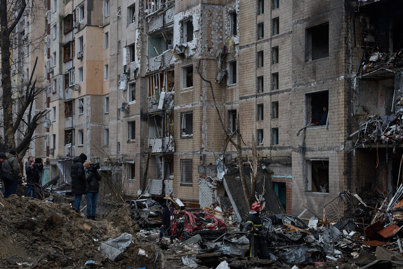 Civilians survey damage to a residential apartment building hit by missile strikes during the 2026 Iran war, with destroyed vehicles and debris visible