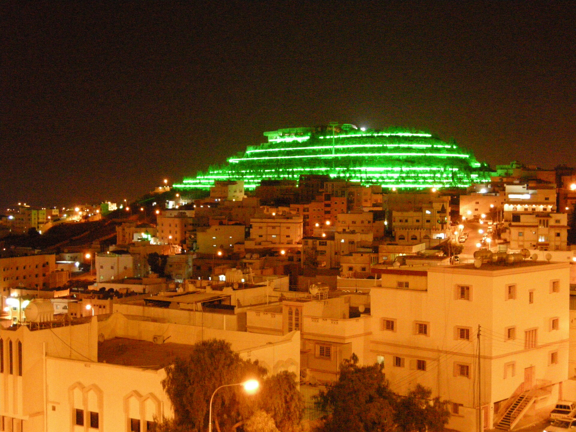 Green Mountain in Abha illuminated with green lights at night, viewed from the city below