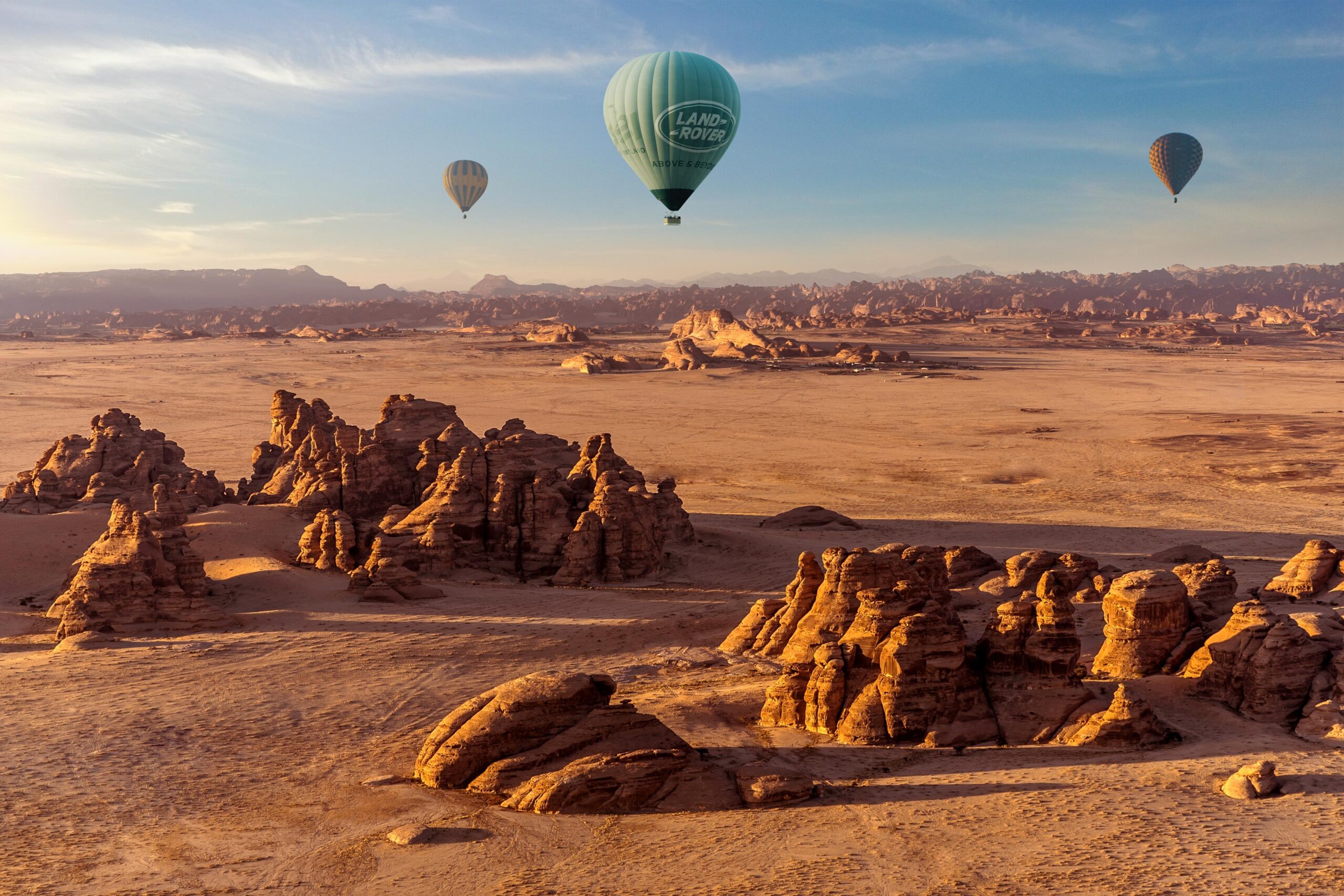 Hot air balloons floating above AlUla's sandstone rock formations at sunrise