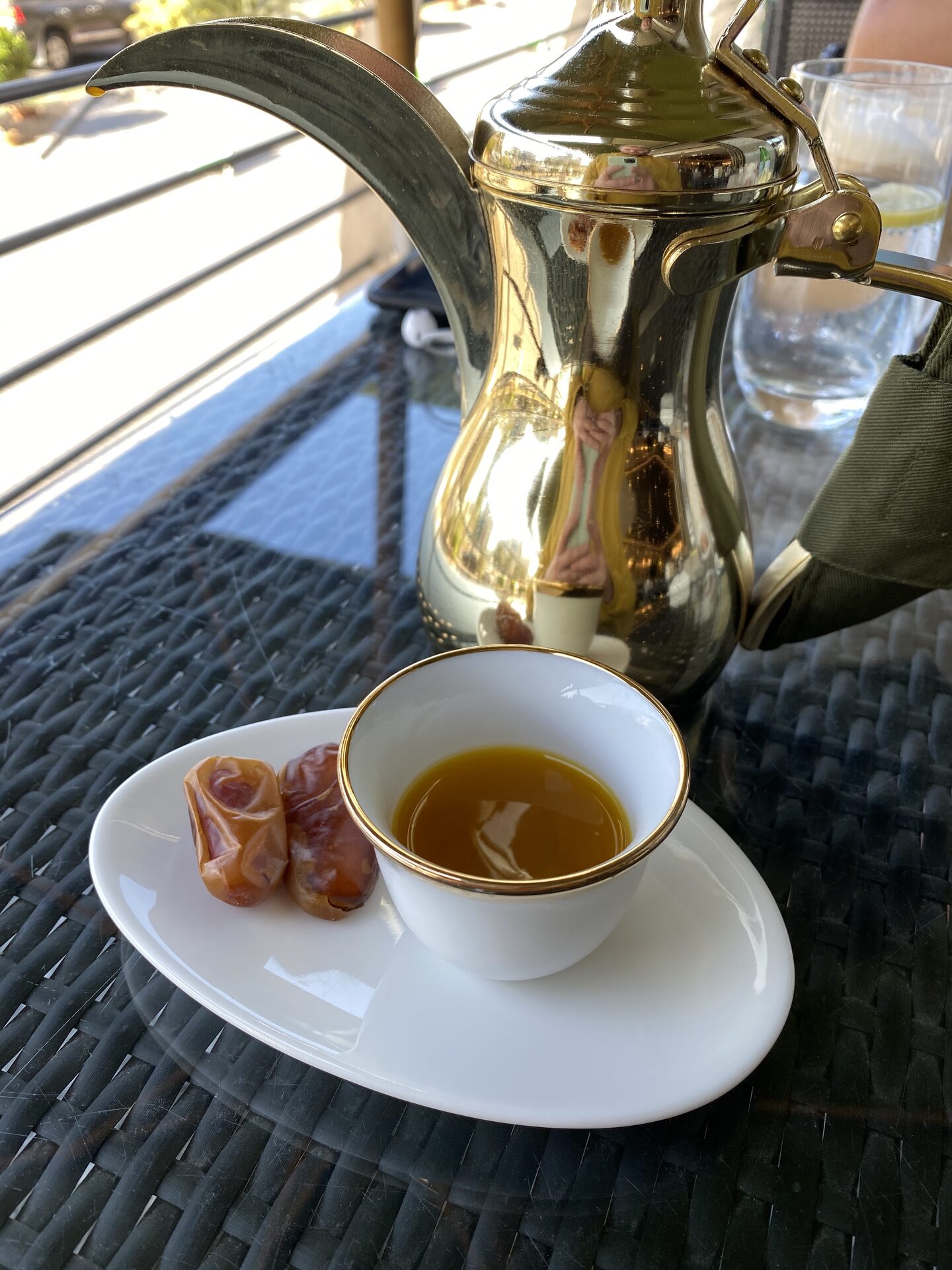 Traditional Arabic coffee (qahwa) being poured from a dallah pot into small cups alongside dates