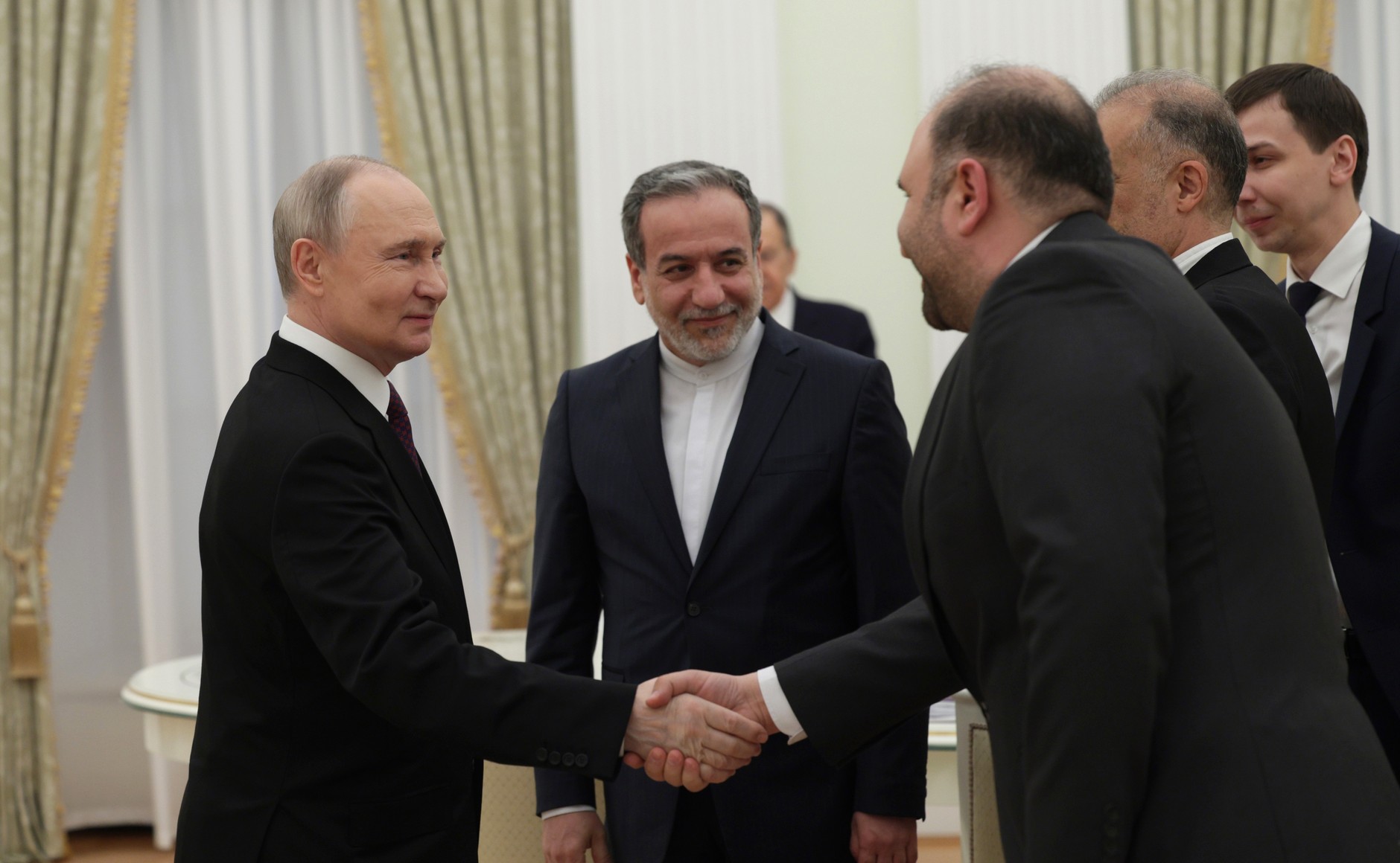Iranian Foreign Minister Abbas Araghchi stands in background as Russian President Vladimir Putin greets the Iranian delegation at the Kremlin, 2025