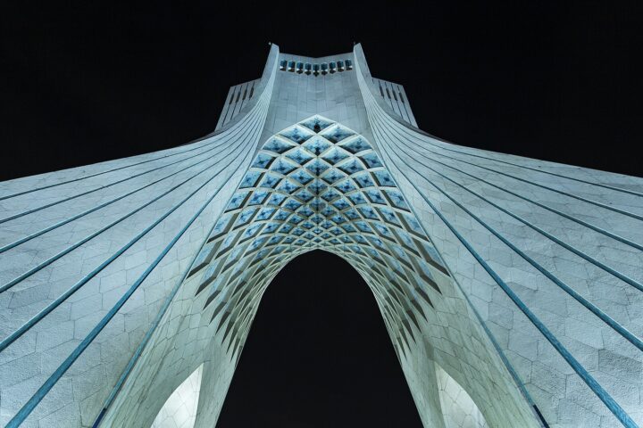 Azadi Tower in Tehran at night — the Islamic Republic capital where Ali Khamenei remains unburied 46 days after the February 28 airstrike, as his successor Mojtaba governs by audio from undisclosed Qom location