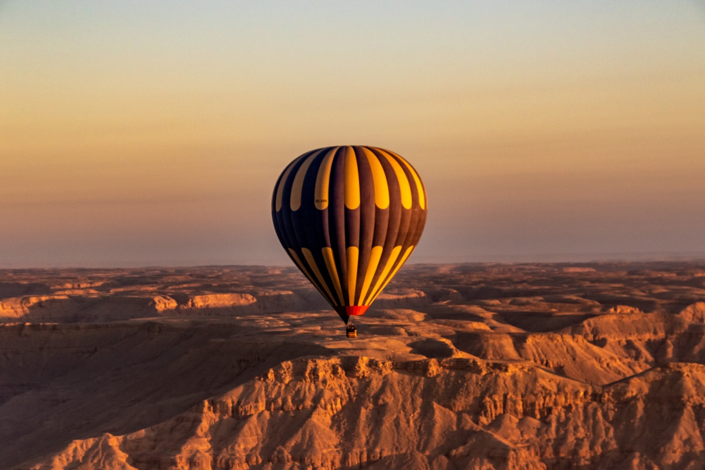 Hot air balloon soaring over golden desert landscape at sunrise, Saudi Arabia