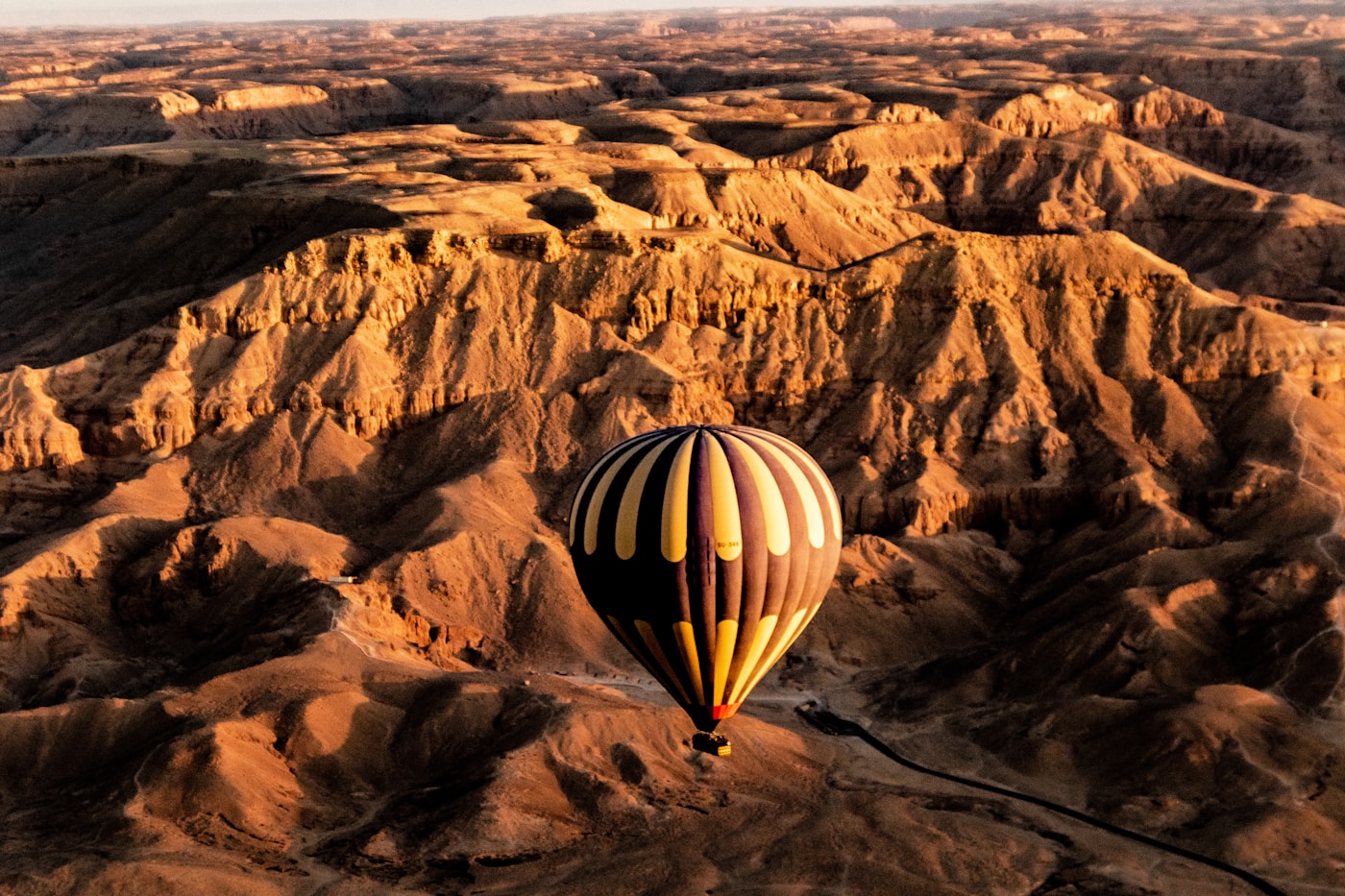 Hot air balloon drifting over red desert terrain at dawn, AlUla Saudi Arabia style landscape