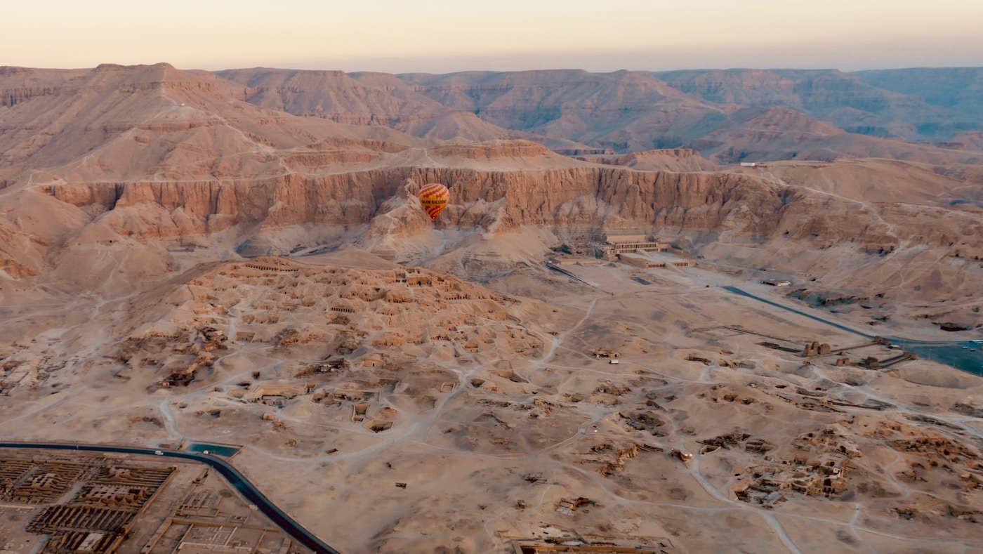 Colourful hot air balloon floating above sandy desert plains at sunrise