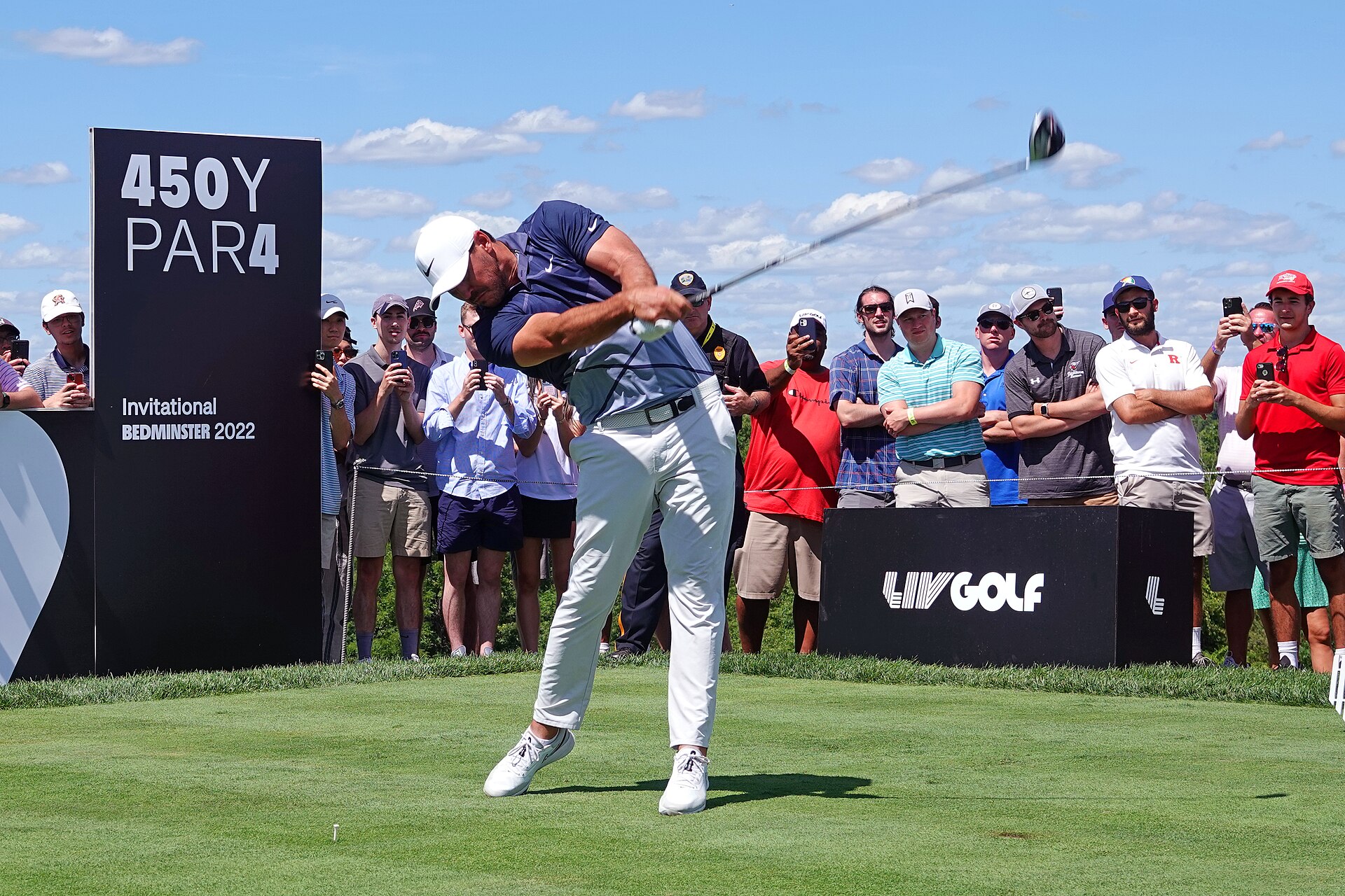 Professional golfer teeing off at a LIV Golf event, with spectators watching from behind the tee box